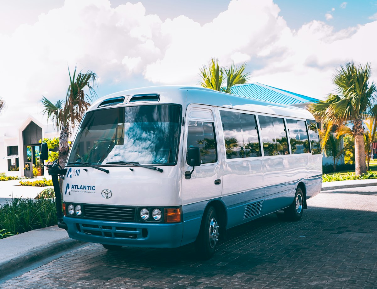 Minibus Toyota Coaster blanc et bleu devant des palmiers